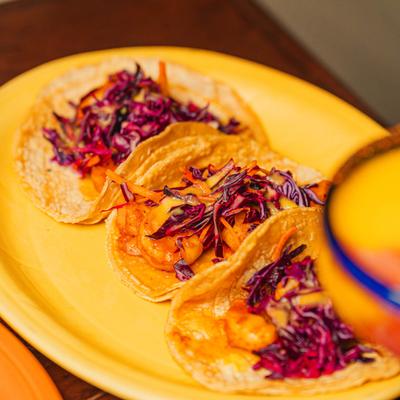 Shrimp tacos topped with purple cabbage on a yellow plate.
