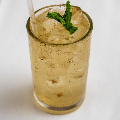 A tall glass filled with a light brown iced beverage sits on a white surface.