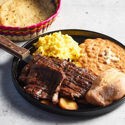 A plate of Carne Asada And Eggs, accompanied by a basket filled with tortillas.