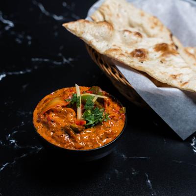 Delhi style butter chicken  bowl served beside a naan basket.