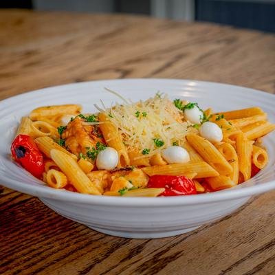 A white plate of Buffalo Chicken Pasta sits on a wooden table.