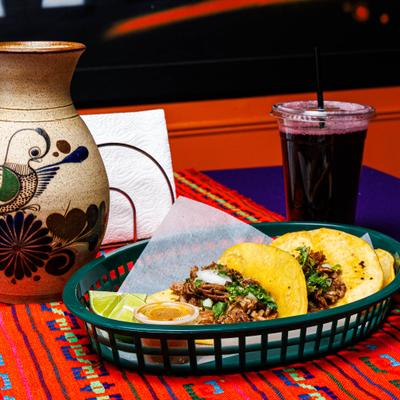 Carnitas Tacos served in a basket alongsie drink served in a cup and ceramic jug.