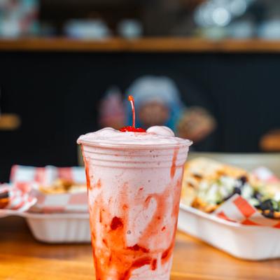 Strawberry Milkshake served in a plastic cup with a cherry garnish.