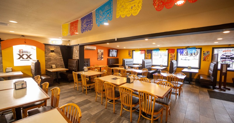 Interior of a restaurant with colorful banners, wooden chairs, and tufted booths