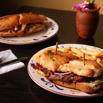 Shuco Puchica sandwich and Pan Con Carne on a table with a clay mug cocktail.