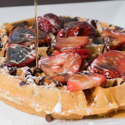 Waffle topped with strawberries, vanilla and chocolate sauce, and powdered sugar.