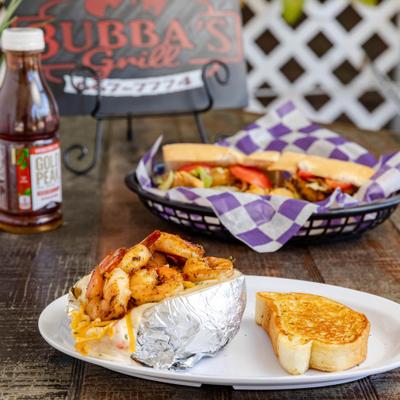 Loaded baked potato topped with shrimp, alongsid a sandwich and bottle of Iced Tea.