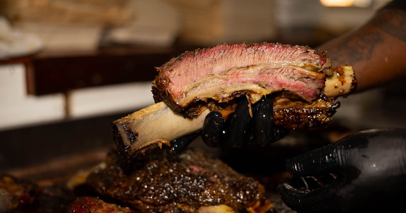 Hands in black gloves holding a medium-rare beef rib