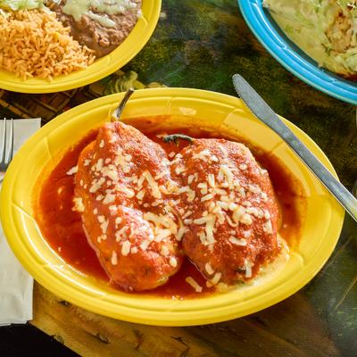 Chile Relleno covered in red sauce and cheese on a bright yellow plate.