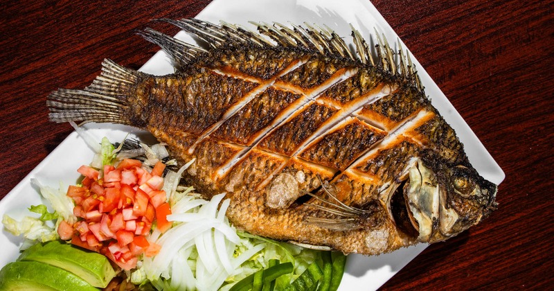 Whole fried mojarra on a white plate with chipped vegetables