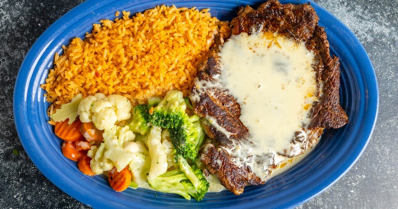 Rib eye steak served with rice and vegetables, and topped with cheese dip