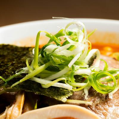 Close up of a sheet of nori and thinly sliced green onion as topping on spicy ramen.