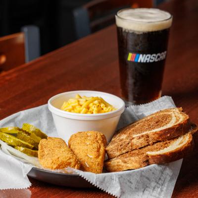 Cod sandwich with mac and cheese, pickle, and Michelob Amber Bock Draft.
