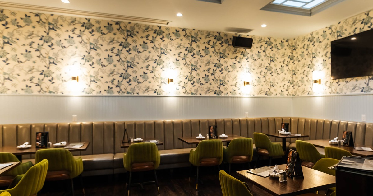 Restaurant interior with floral wallpaper, olive green chairs, and a tufted bench