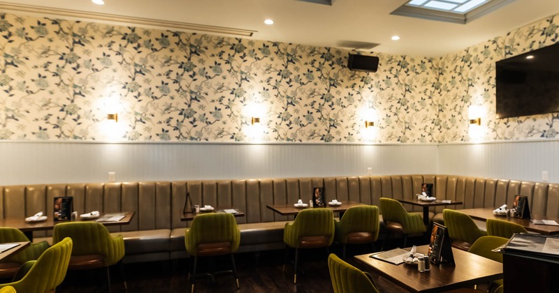 Restaurant interior with floral wallpaper, olive green chairs, and a tufted bench