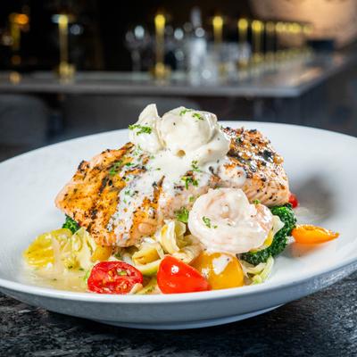 Salmon fillet topped with a creamy white sauce and shrimp, served over pasta.