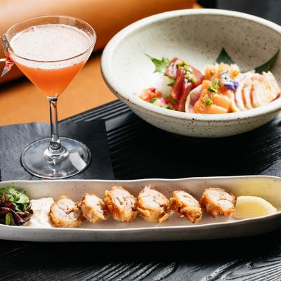 Chicken Karaage served with a cocktail and sashimi on a black table.