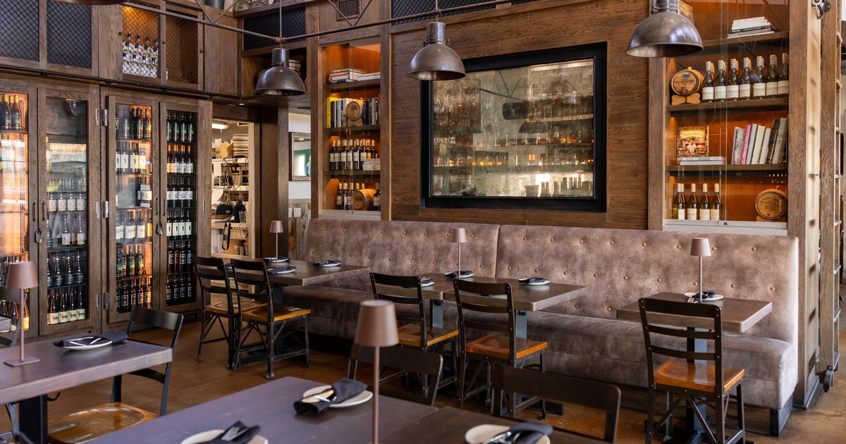 Modern restaurant interior with wooden tables, black chairs, and a brown banquette