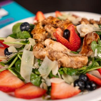 Berry Spinach Salad topped with grilled chicken and shaved cheese, close-up.