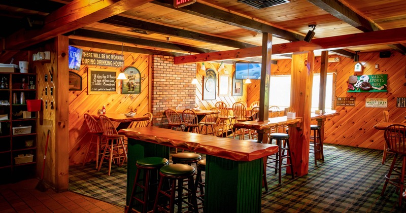 Interior of a bar with wooden and brick decor, high tables, stools, and wall signs