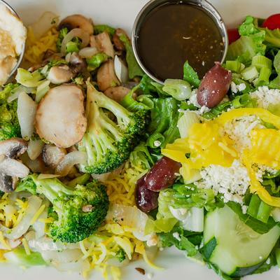 Platter featuring a side of fresh Greek salad alongside seasoned rice and vegetables..