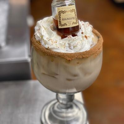 Dessert cocktail with whipped cream, small bottle, and cinnamon-sugar rim.