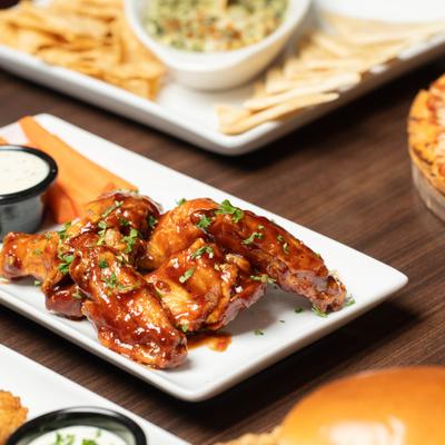 Barbecue chicken wings on a white plate with dipping sauce and carrots.