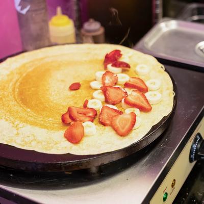 Crepe on the griddle, with bananas and strawberries.