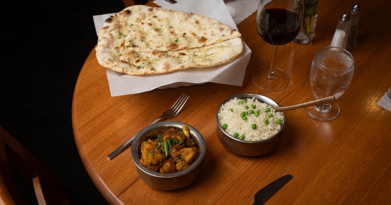 Indian dishes with naan, curry, rice, and red wine on a wooden table