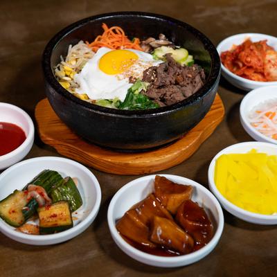 Grilled marinated beef served in a stone bowl, surrounded with assorted side dishes.