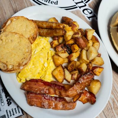 Breakfast platter with potatoes, bacon, sausage, eggs, and toast.