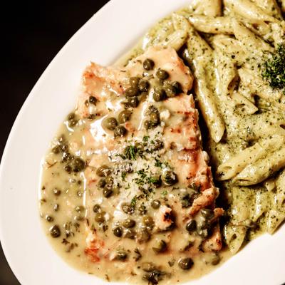 Salmon Piccata served alongside penne pasta tossed in a green pesto sauce.