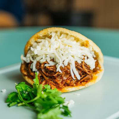 Beef and cheese arepa garnished with parsley.