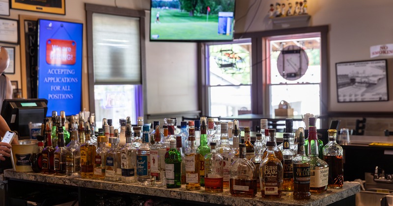 A bar, a pile of drink bottles on it, a TV screen above