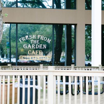 Storefront with white railing, tall columns and glass windows with a sign.
