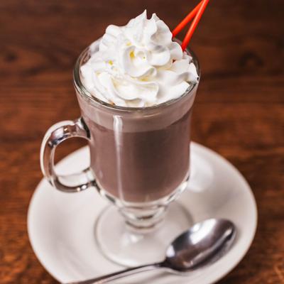 Hot chocolate in glass mug, topped with whipped cream.