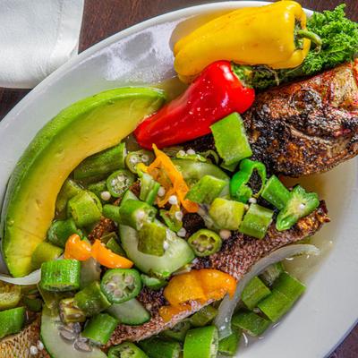 Cooked whole fish covered with greens vegetables, avocado slice, red and yellow bell peppers