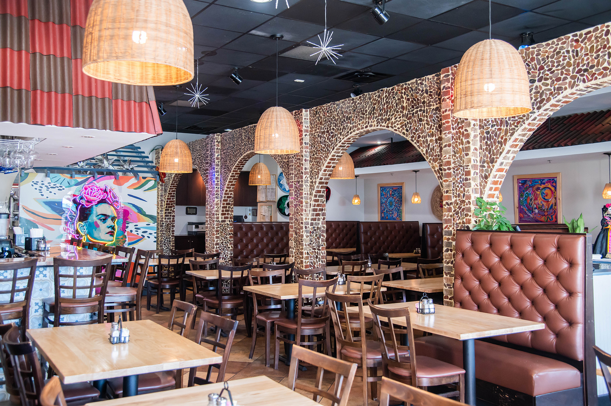 Interior with arched walls, tables, rattan pendant lights, and a vibrant mural