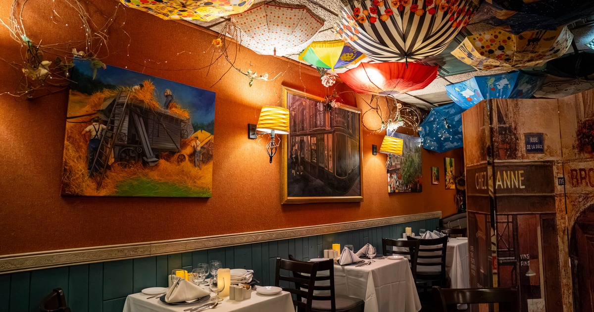 Interior of a restaurant featuring paintings, colorful hanging umbrellas, and two set dining tables