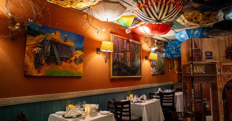 Interior of a restaurant featuring paintings, colorful hanging umbrellas, and two set dining tables