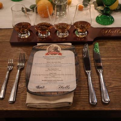 A dining table set with a menu, silverware, and a whiskey flight.