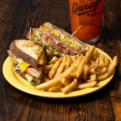 Turkey Club sandwich with fries, served alongide a cocktail.