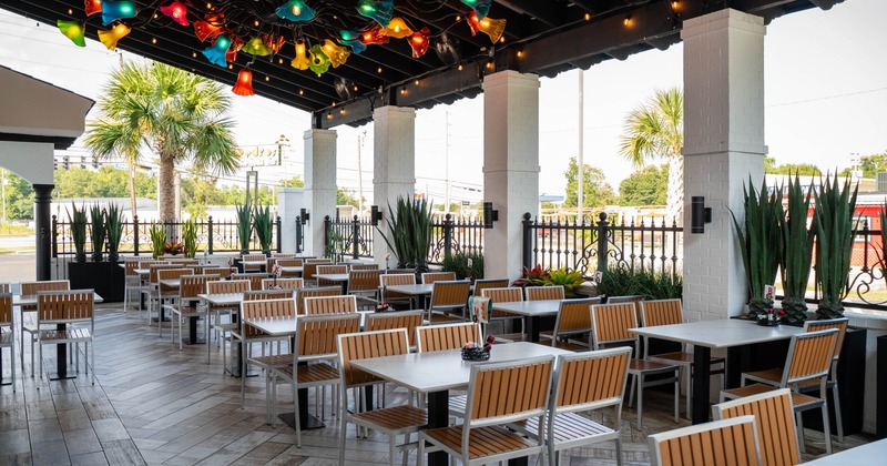 Outdoor dining area with tables, wooden chairs, colorful flower-shaped lights and greenery