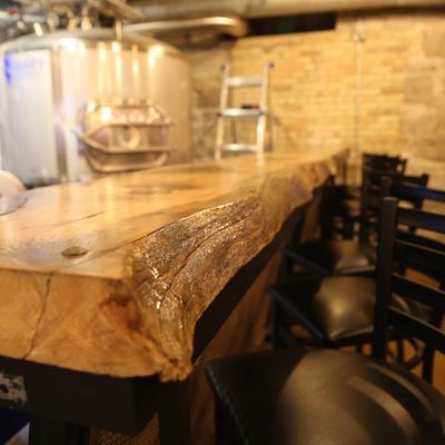Natural wood bar table with chairs, brewery tanks in the background.