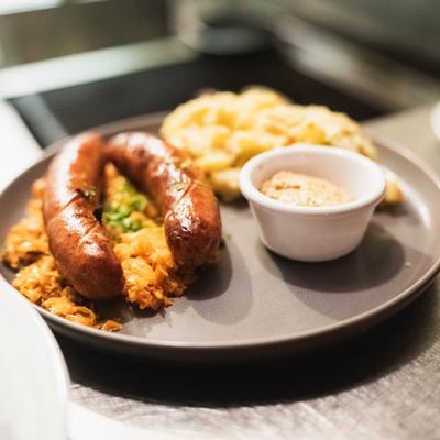 A plate featuring two sausages, sauerkraut, potato salad, and mustard.