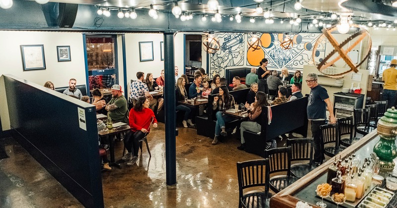 The dining area, tables and chairs, restaurant booths, and a bar on the right. People having fun.