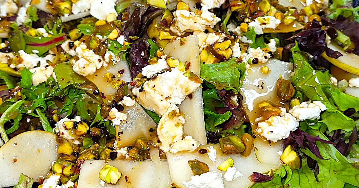 A vibrant salad with mixed greens, sliced pears, crumbled feta, and other ingredients