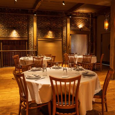 Dining room with elegantly set round tables and brick walls.