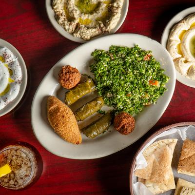 A plate with with veggie grape leaves, kibbe and falafel, surrounded by dip plates and pita.