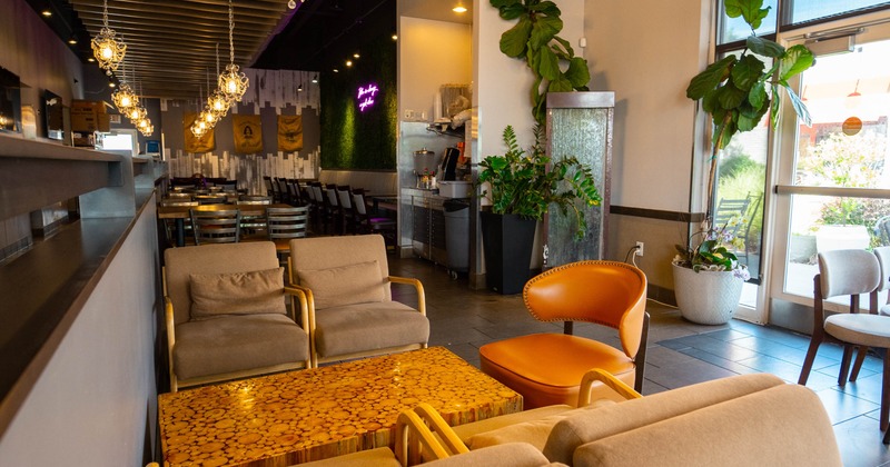 Interior view of a cozy cafe with beige and orange chairs, a wooden table, plants, a water feature